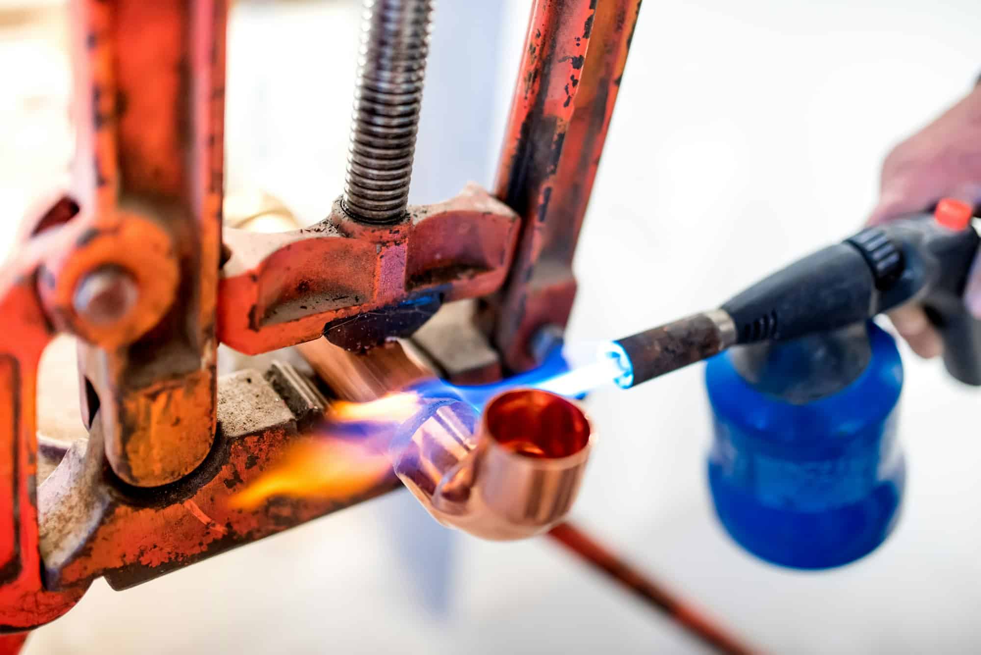 industrial worker using propane gas torch for soldering copper pipes.